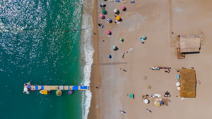 Oludeniz, Turkey. Top down aerial drone flight along shoreline of Oludeniz Beach, colorful umbrellas, crowded pebble coast, waves and pontoon pier, summer.. Aerial View © Video Render
