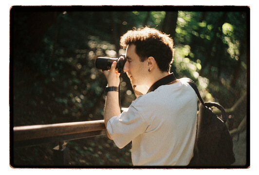A young man shoots with a film camera in dappled forest light