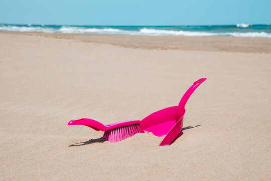 a close-up of a pink dustpan and brush lying on the sand at a beach