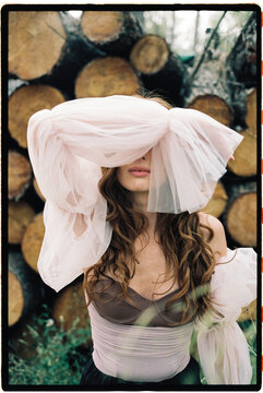 Woman hiding face with pink tulle in forest