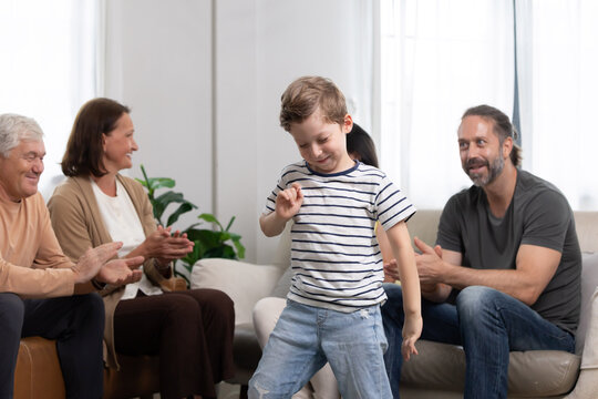 Child performs dance in living room while family watches and claps during gathering in afternoon