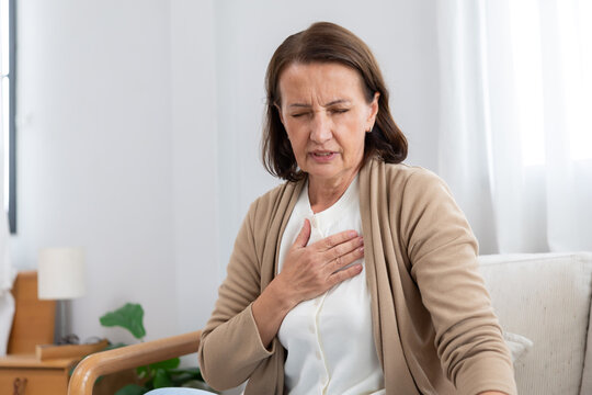 Mature woman holding her chest suffer from heart disease on a couch