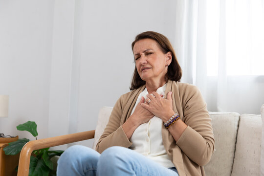 Mature woman holding her chest suffer from heart disease on a couch
