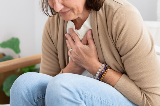 Mature woman holding her chest suffer from heart disease on a couch