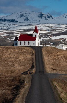 Scenic asphalt road leading to the historic red-roofed Ingjaldsholskirkja church in Snaefellsnes, Iceland