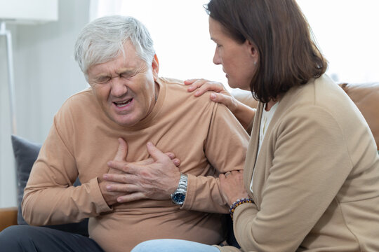 Older woman comforts man holding his chest suffer from heart disease on a couch