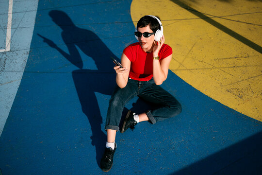 Woman enjoying music with headphones and smartphone on colorful court