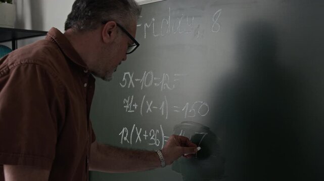 Middle aged Caucasian male teacher writing math equations on chalkboard and explaining lesson. Video for e-learning promos and online school advertising