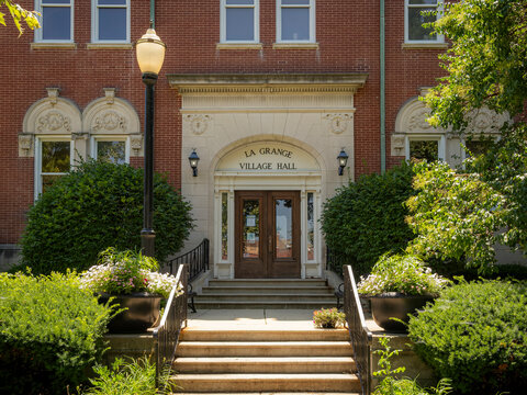 Historic red brick facade and arched entrance of the La Grange Village Hall municipal building on a sunny day with green landscaping and steps