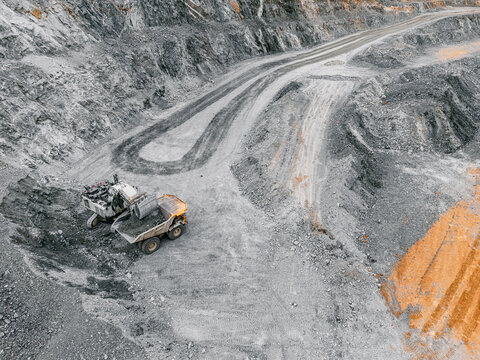 Aerial open pit quarry with haul roads and excavator loading articulated dump truck for mining site background and industrial landscape