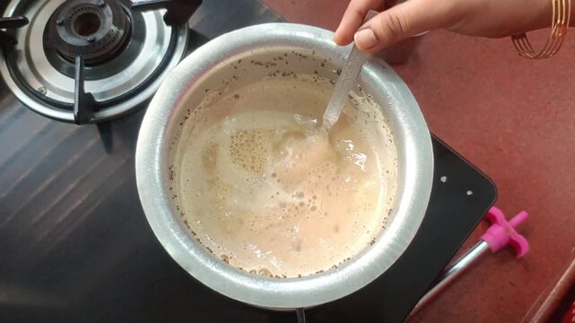 Close up of making traditional Indian masala chai, boiling milk tea with ginger and spices on a gas stove
