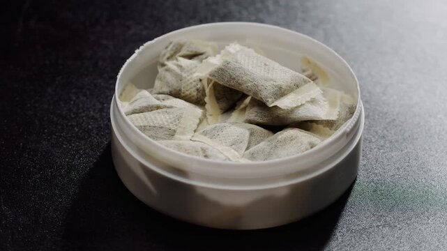 Snus nicotine tobacco close up, pack of tobacco for gum. unhealthy addiction. Man opening box with snus and taking one.