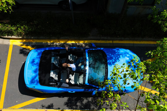 A stylish Asian girl sleeps inside a blue convertible.