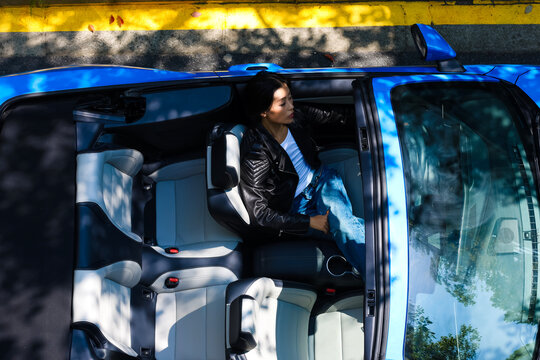 A stylish Asian girl sleeps inside a blue convertible.