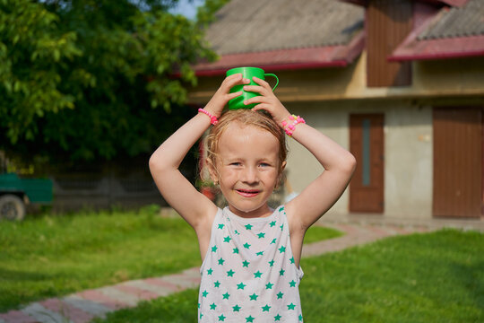 Little smiling girl holding a green cup on her head, Carefree summer, summer vacation and healthy lifestyle of children