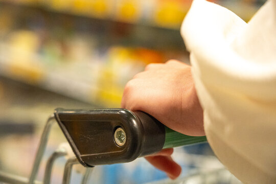 A Close-Up of a Hand Grasping a Shopping Cart Handle in a Supermarket Aisle Filled with Colorful Products and Groceries Ready for Selection
