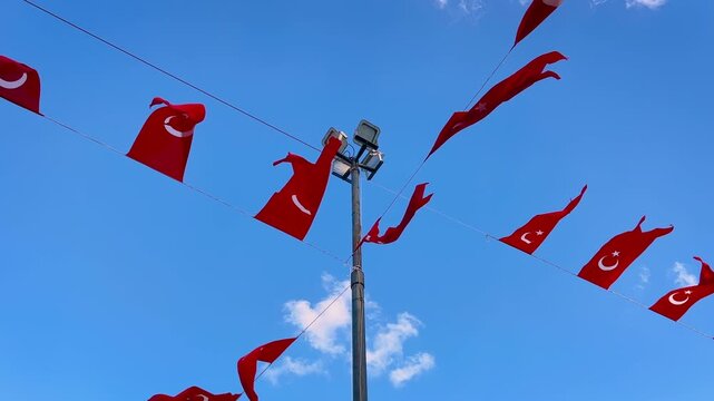 Multiple Turkish national flags stretched on wires, waving in strong wind against blue sky with clouds. Concept of national identity, patriotism, public decoration and state symbolism.