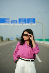 Fototapeta premium Woman adjusts sunglasses while standing confidently on an open highway