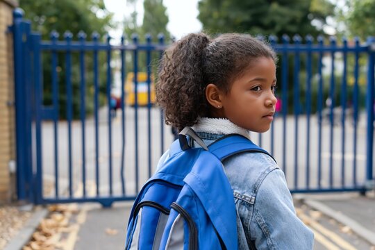 Girl with backpack standing outside school gate looking back, back to school photo