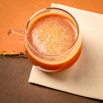 glass cup of fresh home made carrot juice on a napkin against colorful paper abstract, healthy eating concept