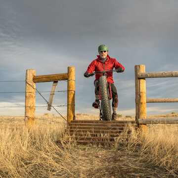 senior male is riding a mountain fat bike and approaching a cattle guard in Soapstone Prairie Natural Area in northern Colorado, late fall scenery