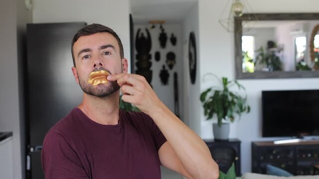 Handsome adult man applying funny golden lip mask