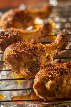 baked bbq chicken drumsticks on metal wire rack, crispy golden brown skin and dripping juices in close-up and soft focus