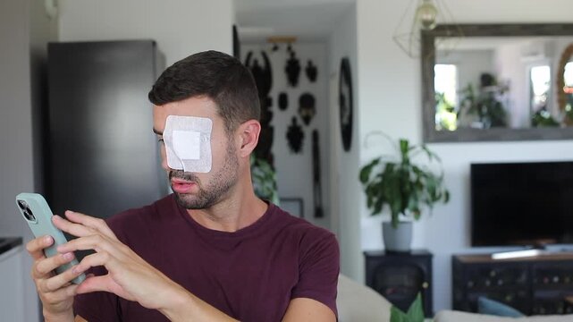 Man with large patched eye experimenting vision problems while looking at his mobile phone 