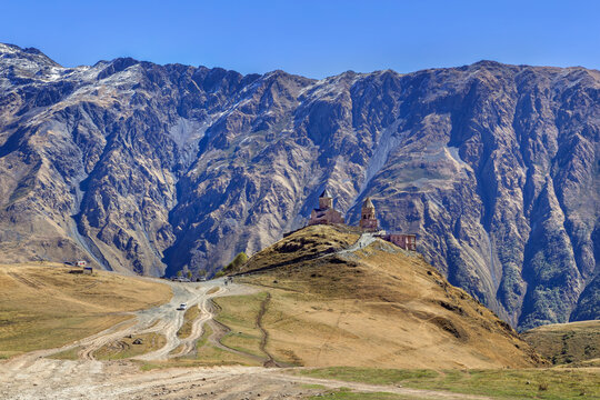 Gergeti Trinity Church stands against Caucasus mountains in Georgia. Scenic distant back view under bright morning sky