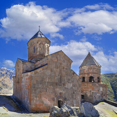 Fototapeta premium Gergeti Trinity Church and historic bell tower stand inside stone courtyard, Georgia. Square composition in daylight