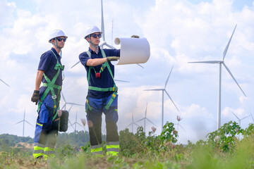 Engineers review plans at wind farm during daylight hours while wind turbines stand in the background © Freeday photo