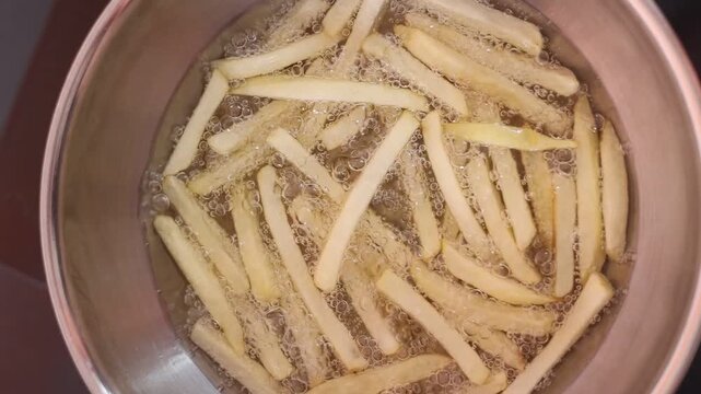 Close-up video of French fries deep frying in hot cooking oil, golden potato strips bubbling in a pan during food preparation in a commercial kitchen.z