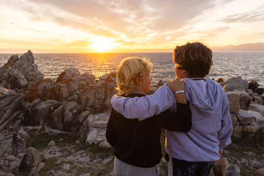 two boys exploring and hiking the spectacular rocky coastline of DeKelders, South Africa at sunset