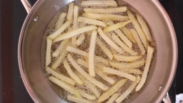 Close-up video of French fries deep frying in hot cooking oil, golden potato strips bubbling in a pan during food preparation in a commercial kitchen.z