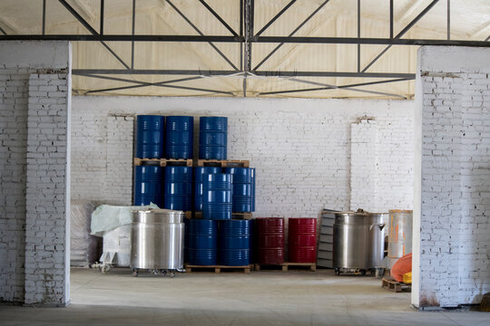 In the center of the room, stacks of blue and red metal barrels are compactly placed on wooden pallets, which is typical for the logistics of chemical production.