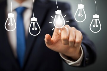 Businessman pointing at a glowing idea light bulb icon representing innovation creativity and problem solving © Tahmina