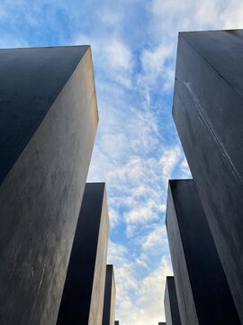Abstract architectural concept of dark concrete geometric monoliths looking up toward a cloudy sky