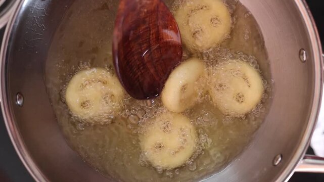 Close-up video of smiley face potato snacks deep frying in hot cooking oil, bubbling oil cooking frozen potato bites until golden and crispy.