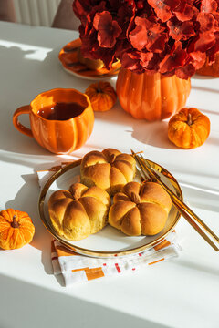 Pumpkin-shaped bread rolls with autumn decoration and hot drink