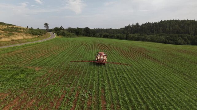 Agricultural tractor applying pesticide or fertilizer to young corn crops