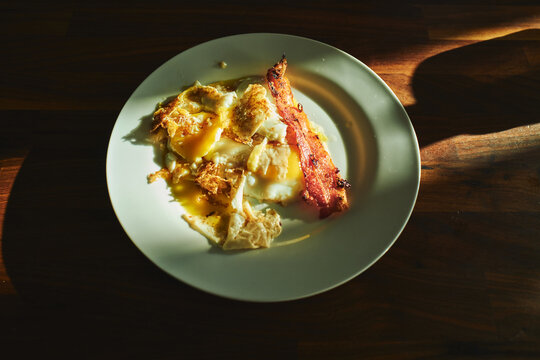 Fried eggs and crispy bacon on a plate in morning sunlight