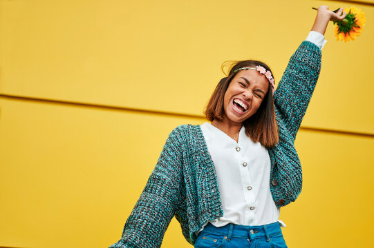 Enthusiastic young woman holding sunflowers and celebrating with yellow background