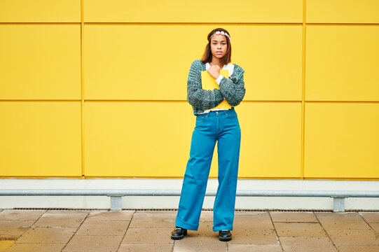 Adult student holding a yellow book and standing in front of a yellow wall