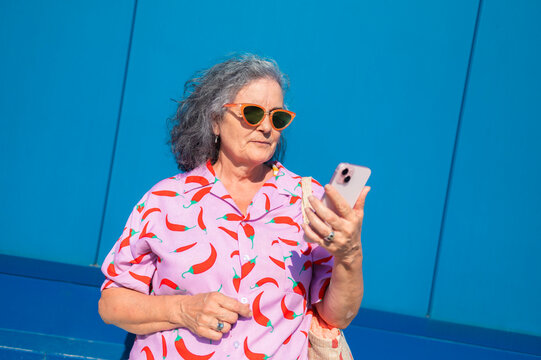 Senior woman using smartphone in front of blue wall