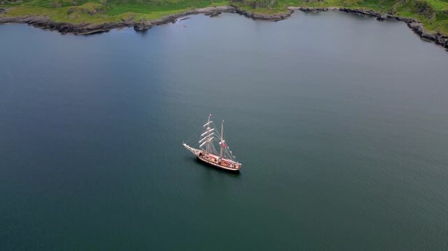 Aerial view of a large sailing ship on calm waters near a green coastline
