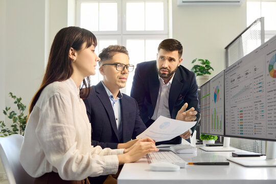 Analysts team reviewing data on computer dashboards. Three colleagues analyze charts in an office, reviewing finance reports on a monitor for planning. Teamwork and analytics drive results.