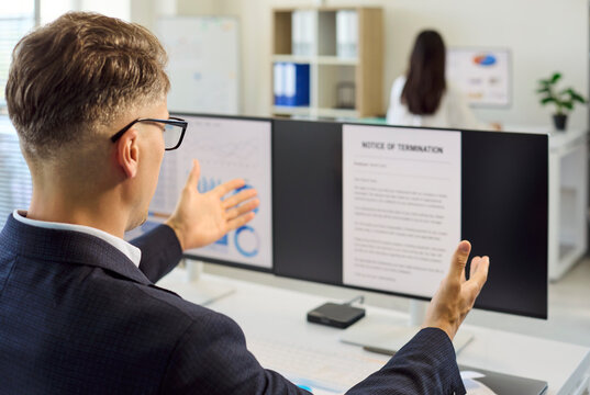 Man employee in office reading termination notice. He reacts with raised hands at a computer screen showing a formal document on dismissal and termination. Symbol of job loss and firing.