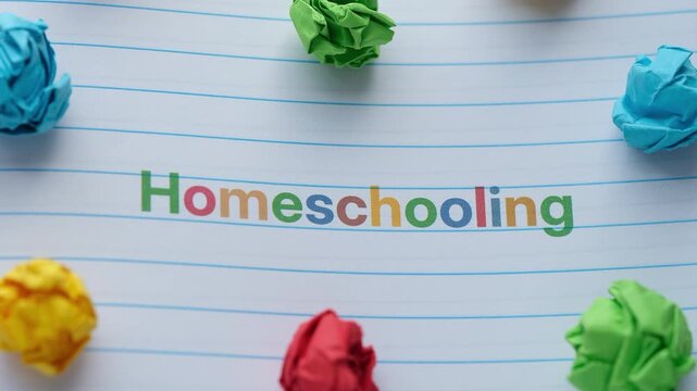 A lined notebook page featuring the word Homeschooling printed in colorful letters, surrounded by paper crumpled balls. Close up. 