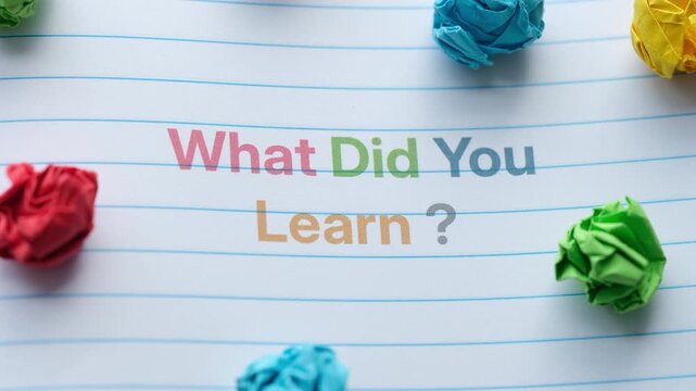 A lined notebook page featuring the question What Did You Learn? printed in colorful letters, surrounded by crumpled paper balls. Close up.
