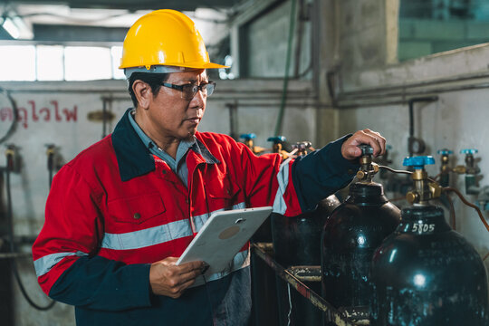 Technician hard hat gas cylinder tablet inspection factory safety worker male technician in red uniform checking industrial gas cylinder valve